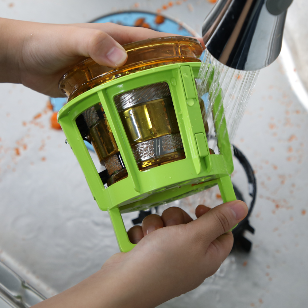 Hands using a green cleaning tool to scrub the juicing strainer.