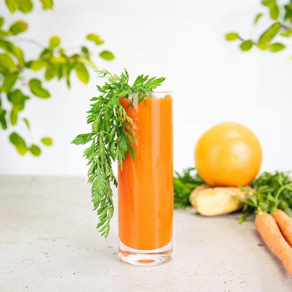 carrot grapefruit juice in a glass with a carrot green garnish