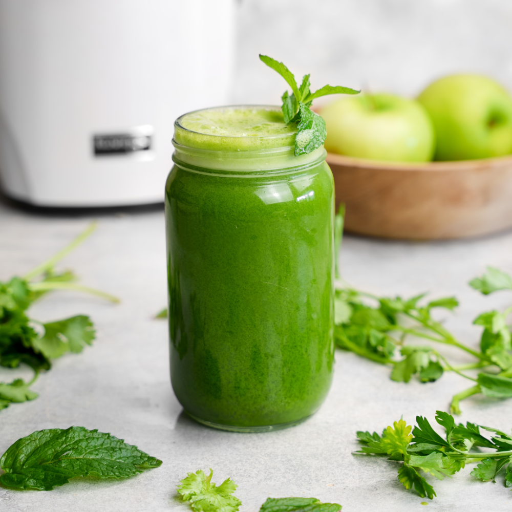 green juice in a mason jar surrounded by cilantro, parsley, and mint leaves